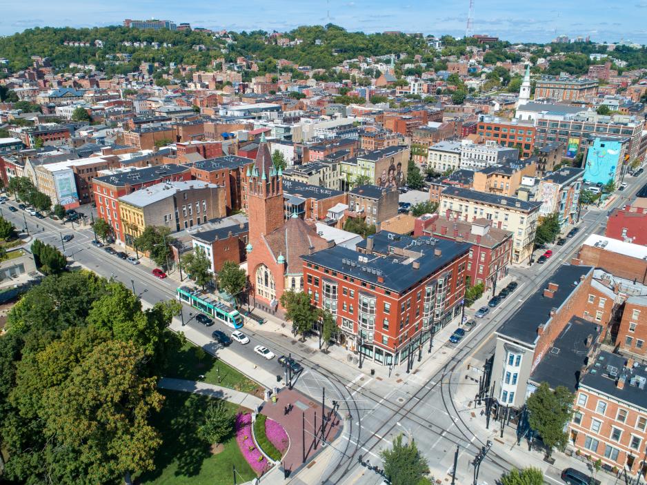 Photo from above of the corner of a city park with several taller buildings and a bus on the roadway between the park and the buildings