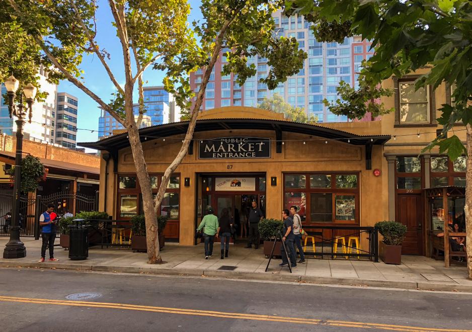 A photo of a restaurant entrance with a people walking on the adjacent sidewalk.