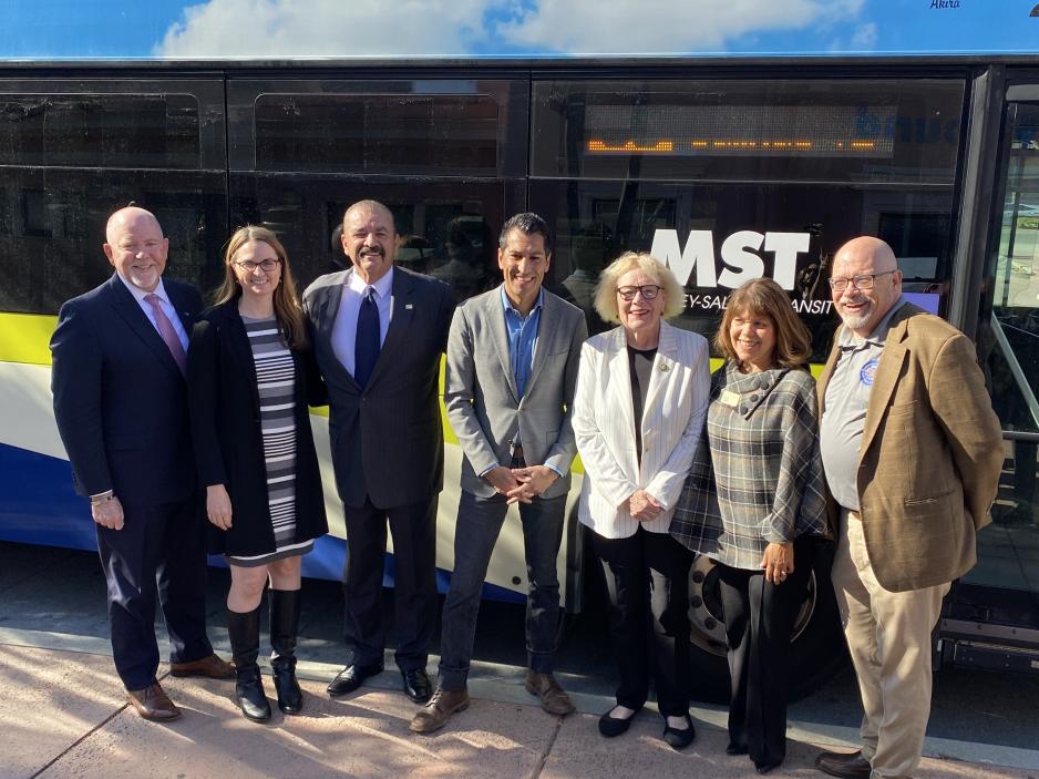 group of elected officials in front of bus